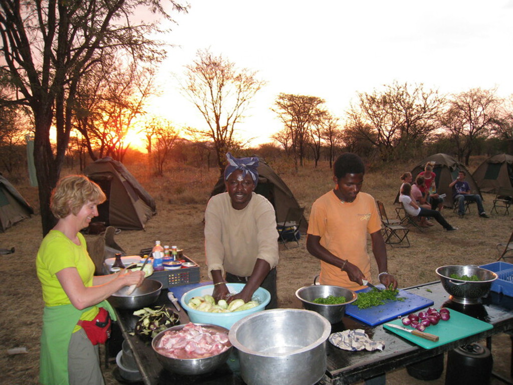 Kampeerkoks bereiden diner bij tentenkamp tijdens groepsrondreis Kenia, Tanzania en Zanzibar bij zonsondergang.