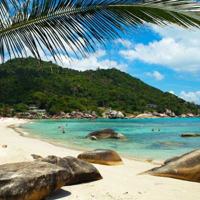 Tropisch strand in Zuid-Thailand met palmbomen, rotsen en helderblauw zeewater tijdens familiereis.