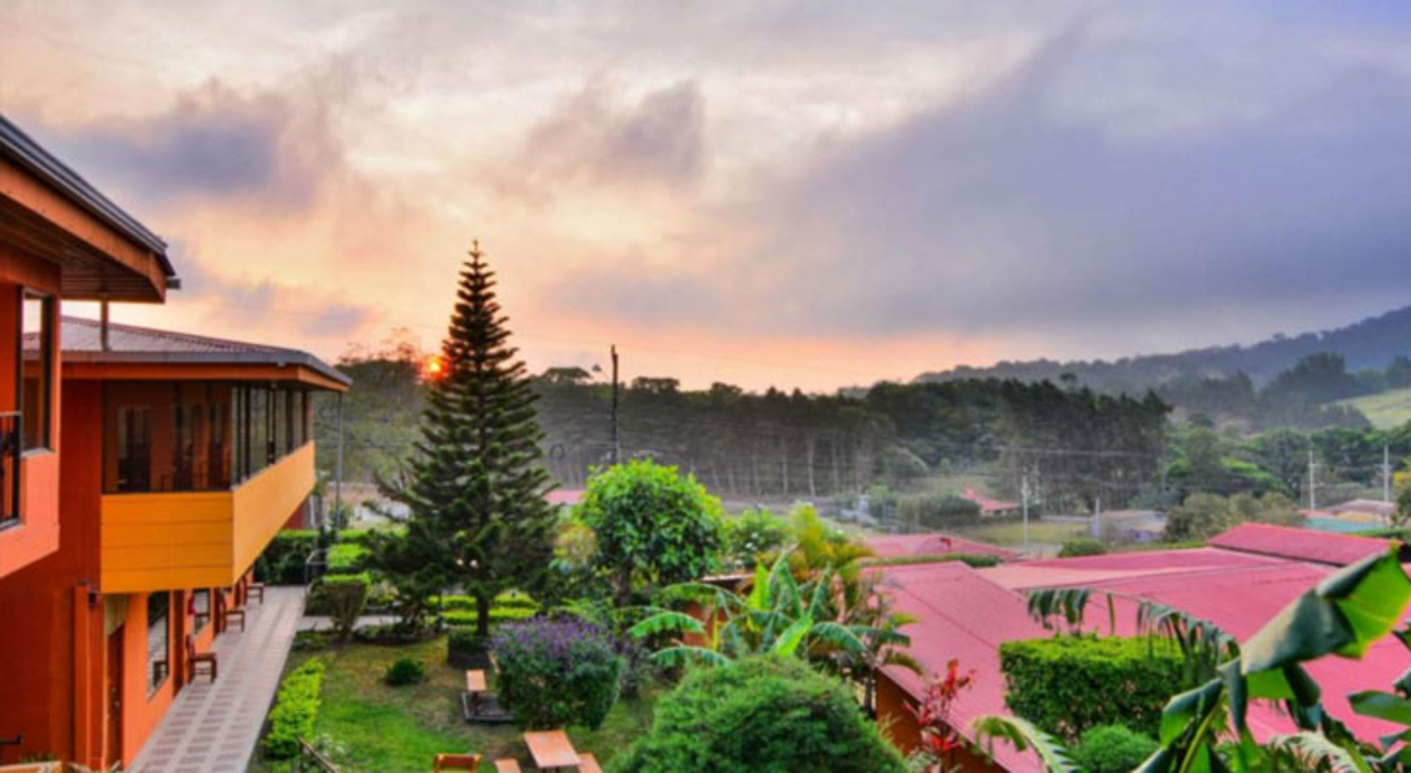 Accommodatie Monteverde Zonsondergang boven groene heuvels en lodge met tropische tuin in Costa Rica.