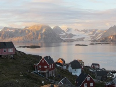Kleurrijke huizen aan de kust met uitzicht op fjord en besneeuwde bergen in Groenland.