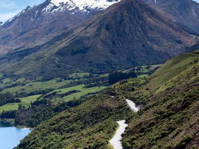 Panoramisch uitzicht op de kronkelende weg bij Queenstown met besneeuwde bergtoppen en een meer, Nieuw-Zeeland.
