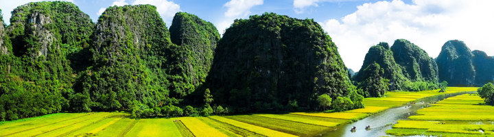 Groene karstbergen en rijstvelden langs een rivier in Vietnam.