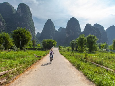 Fietser op landweg tussen rijstvelden en karstbergen bij Yangshuo, Route China.