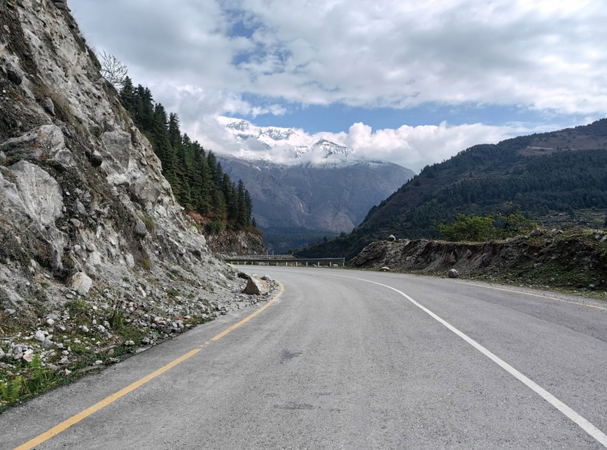 Bergweg door een vallei met dennenbossen en besneeuwde Himalaya-toppen in Nepal.