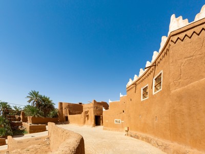 Traditionele lemen gebouwen met palmbomen langs een straat in Saoedi-Arabië.