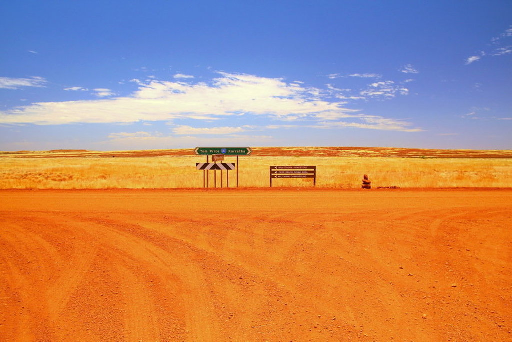 Rode zandweg met wegwijzers in het outbacklandschap van West-Australië onder een blauwe lucht.