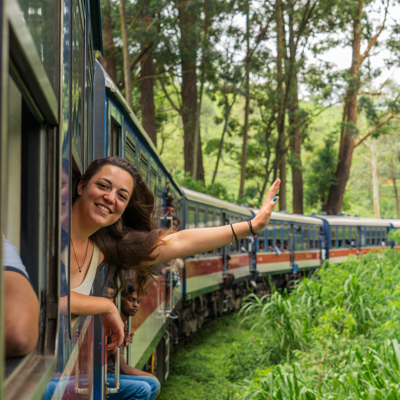 Jonge reiziger zwaait uit de trein tijdens 22-35ers reis Sri Lanka door groen berglandschap.