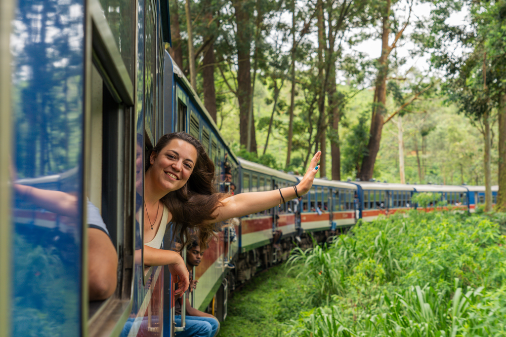 Jonge reiziger zwaait uit de trein tijdens 22-35ers reis Sri Lanka door groen berglandschap.