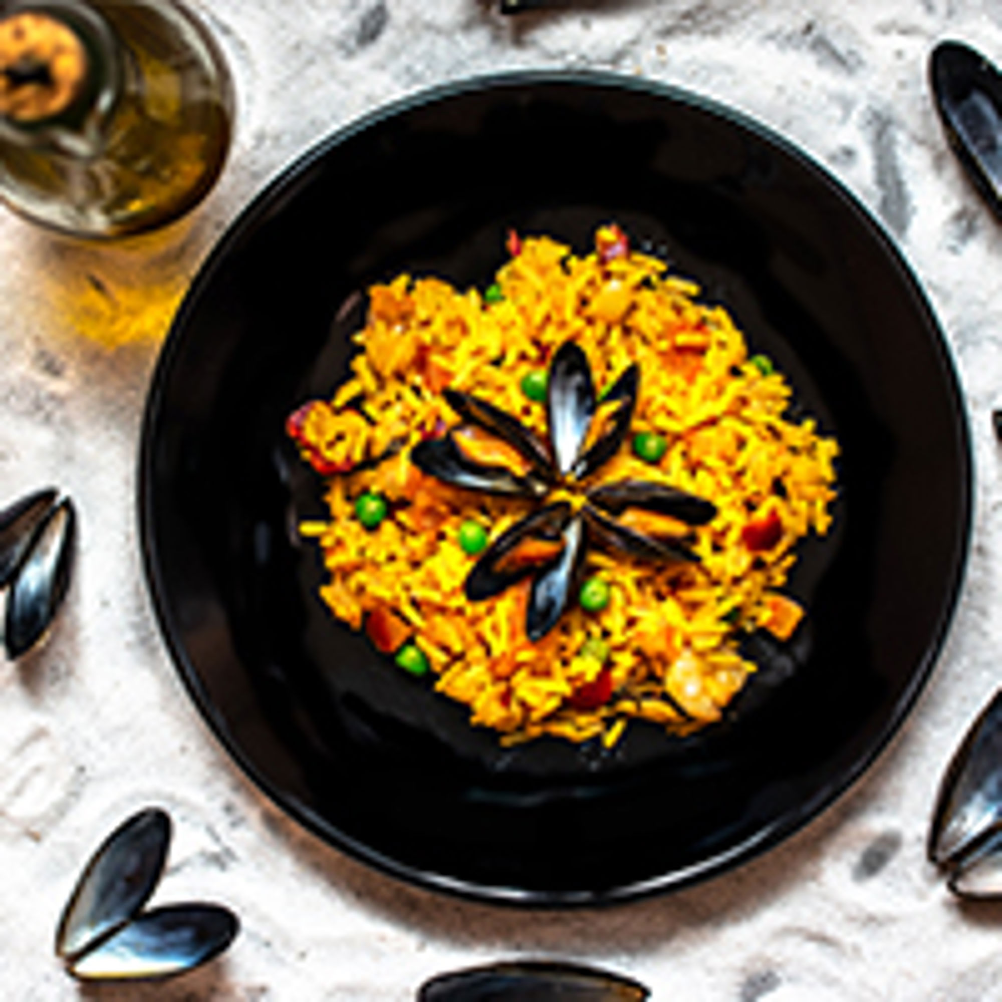 Zeevruchtenpaella met mosselen en erwten geserveerd in een zwarte kom.