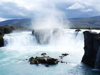 Godafoss-waterval in Noord-IJsland met nevel boven het turquoise water en uitzichtpunten langs de kliffen.