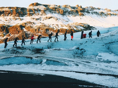 Wandelaars steken een gletsjer over tijdens de 7-daagse wandelvakantie in IJsland, met besneeuwde bergen op de achtergrond.