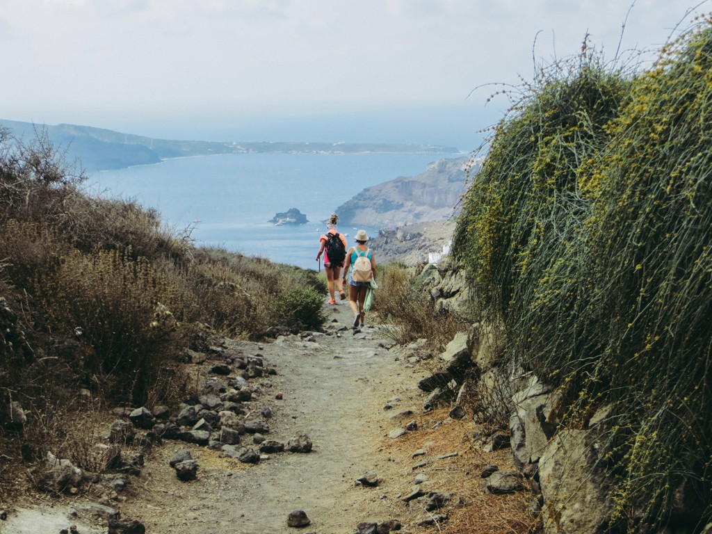 Wandelaars op een bergpad met uitzicht op zee en kliffen tijdens wandelvakantie op Santorini, Griekenland.