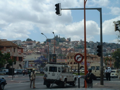 Straatbeeld in Antananarivo, Madagascar, met verkeer, stoplichten en huizen op een heuvel.