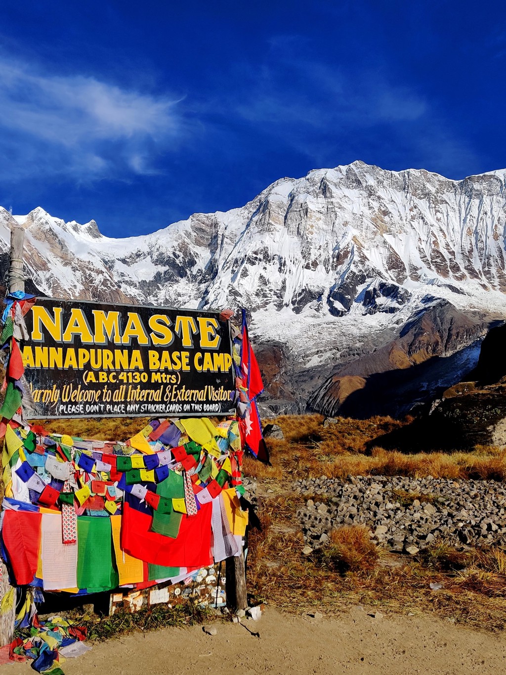 Bord bij Annapurna Base Camp in Nepal met gebedsvlaggen en besneeuwde Himalaya op de achtergrond.