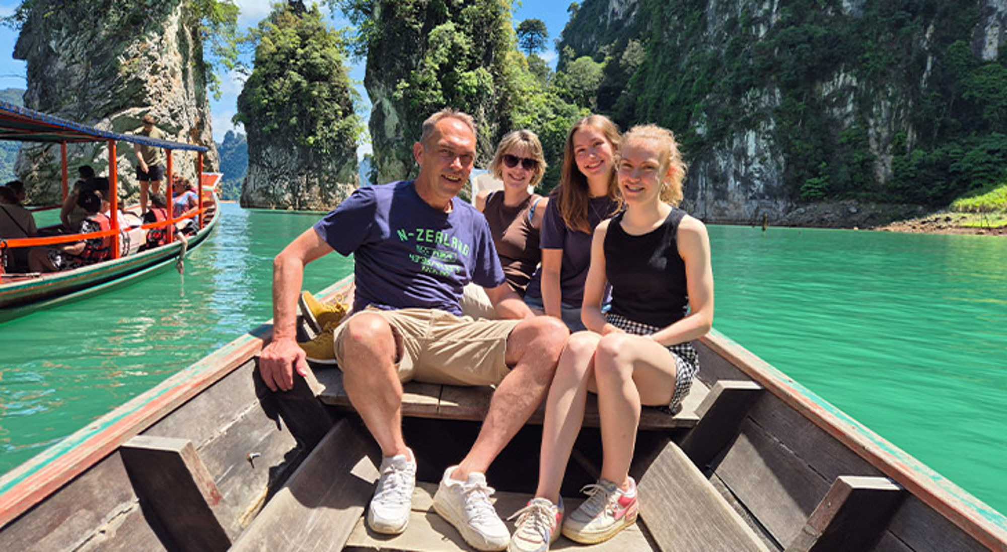 Familiereis Thailand Gezin in een longtailboot op smaragdgroen water tussen kalksteenrotsen en jungle.