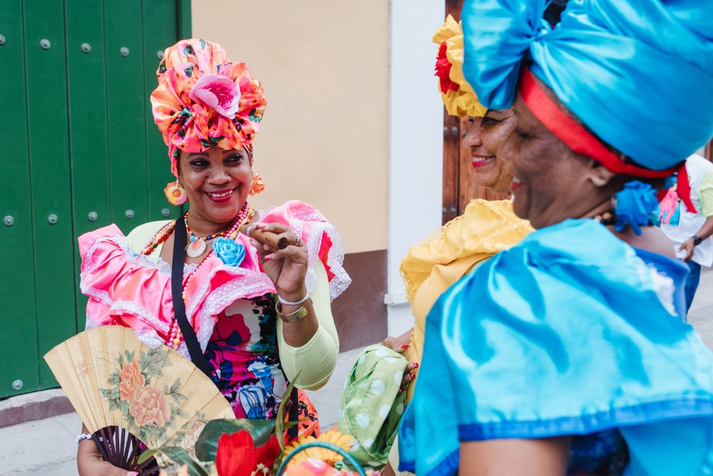 Vrouwen in kleurrijke Cubaanse kleding met hoofddoeken, waaiers en sigaar in een straat in Havana.