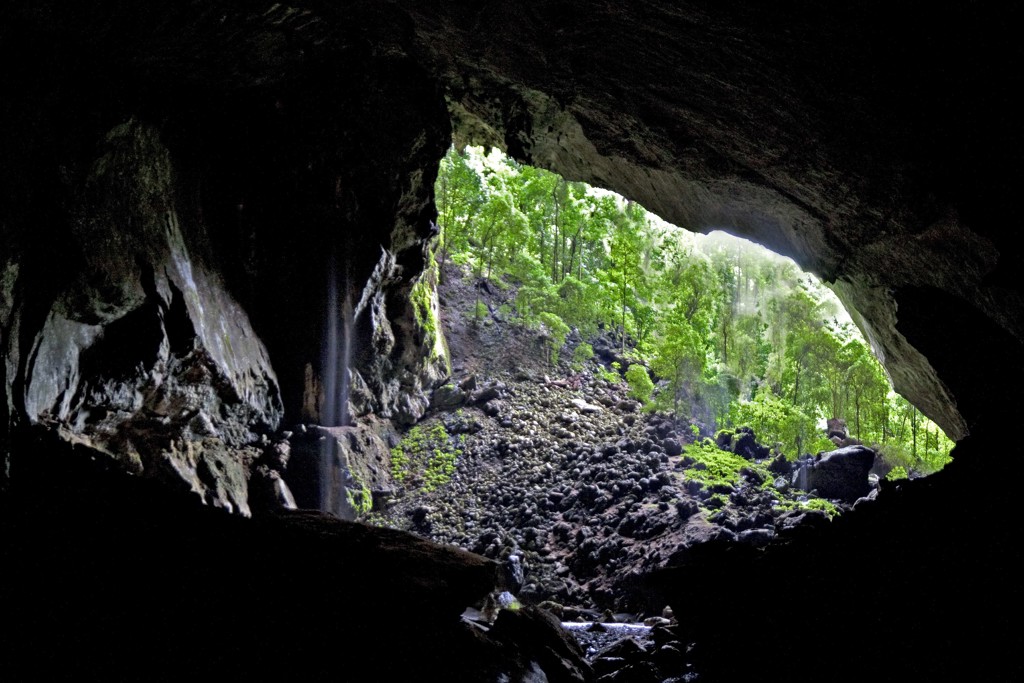 Uitzicht vanuit een grot op het regenwoud van Maleisisch Borneo, met rotsen en een kleine waterval.