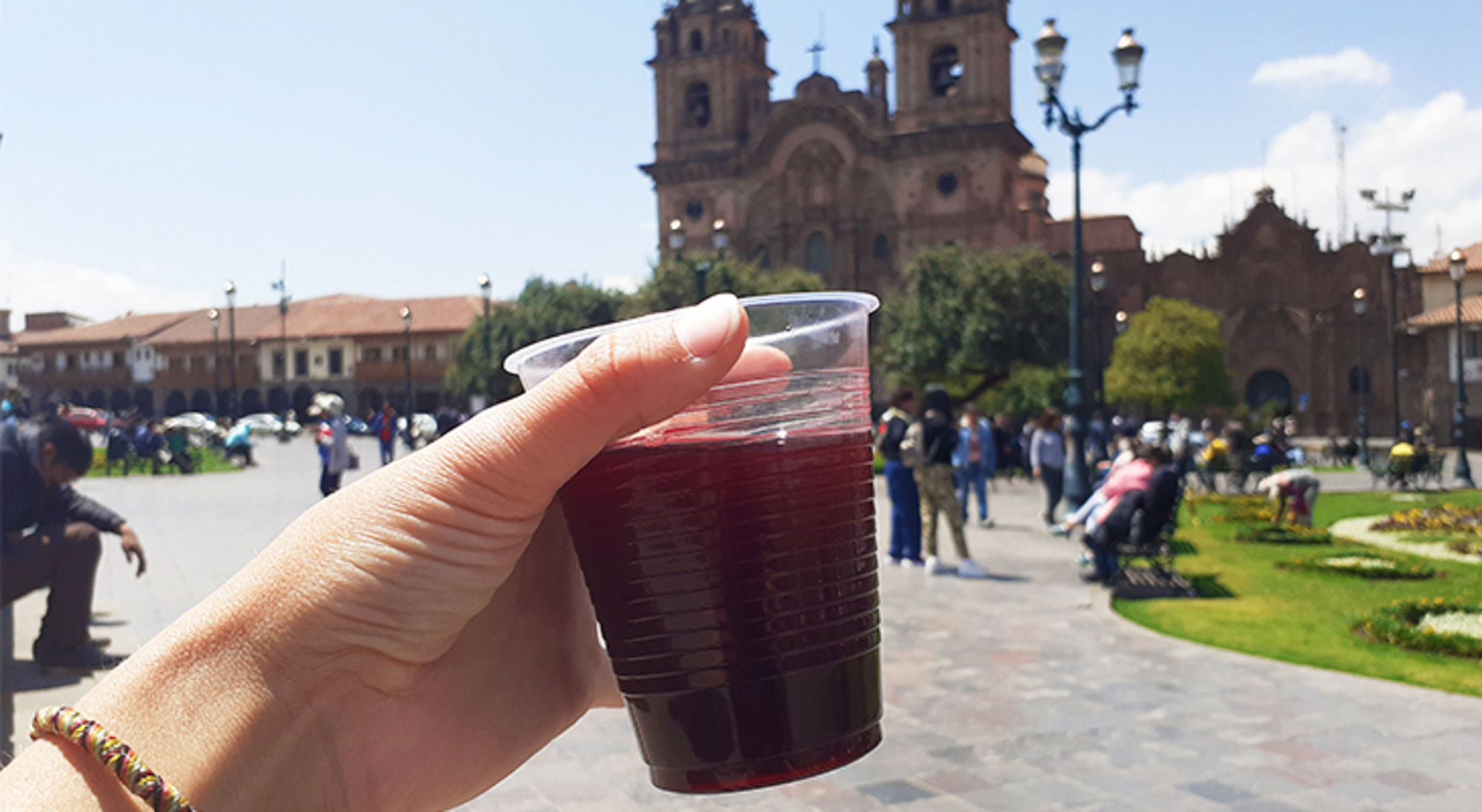 Hand met plastic beker paarse chicha op Plaza de Armas in Cusco, met kathedraal op de achtergrond.
