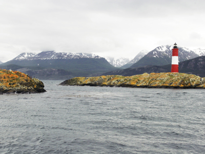 Rood-witte vuurtoren op rotsachtig eiland met besneeuwde bergen op de achtergrond, Route Antarctica.