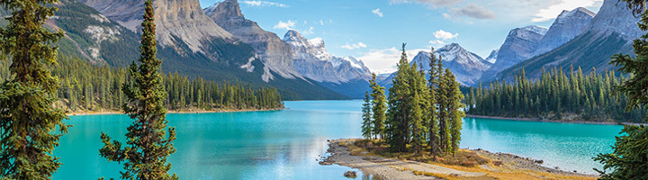 Turquoise bergmeer in Canada met dennenbos en besneeuwde bergtoppen onder een heldere lucht.