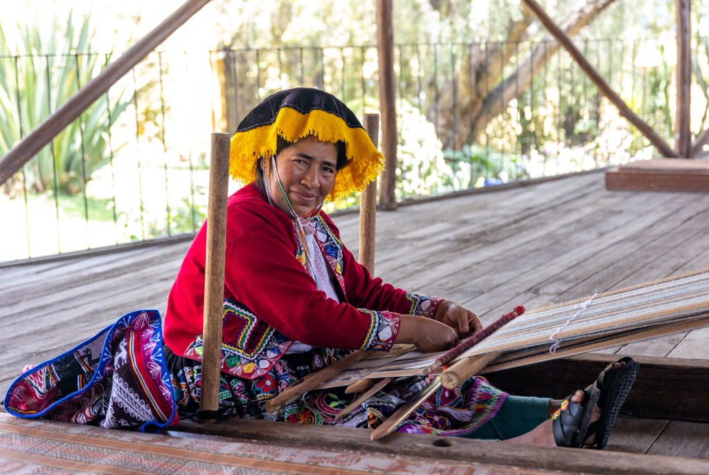 Vrouw in traditionele kleding weeft textiel op een houten weefgetouw tijdens een 22-35ers reis Peru.