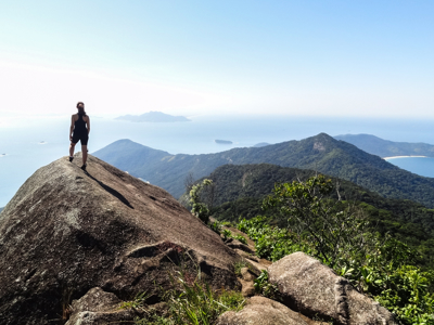 Wandelaar op rotsige bergtop met uitzicht op groene heuvels en zee tijdens de route Brazilië en Buenos Aires.