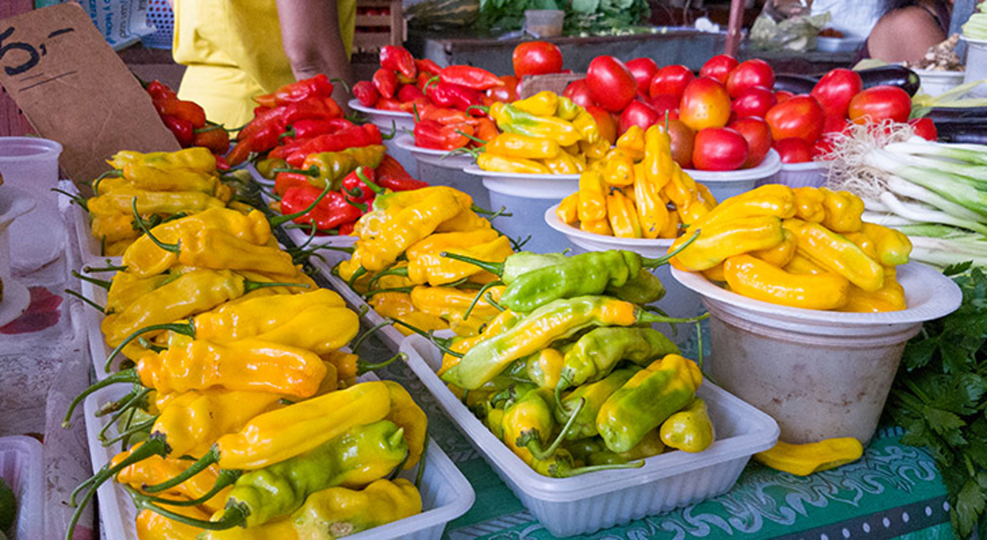 Kleurrijke marktstalletje met gele, groene en rode pepers en tomaten in schalen.