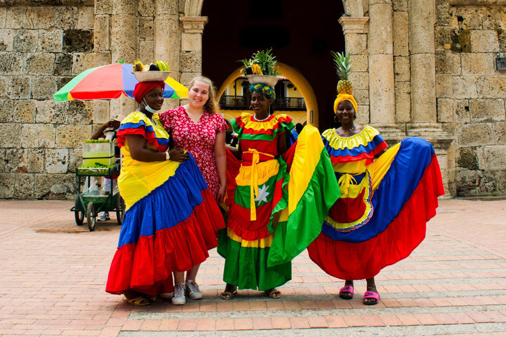 Reiziger poseert met vrouwen in kleurrijke jurken bij historische stadspoort in Colombia tijdens 22-35ers reis.