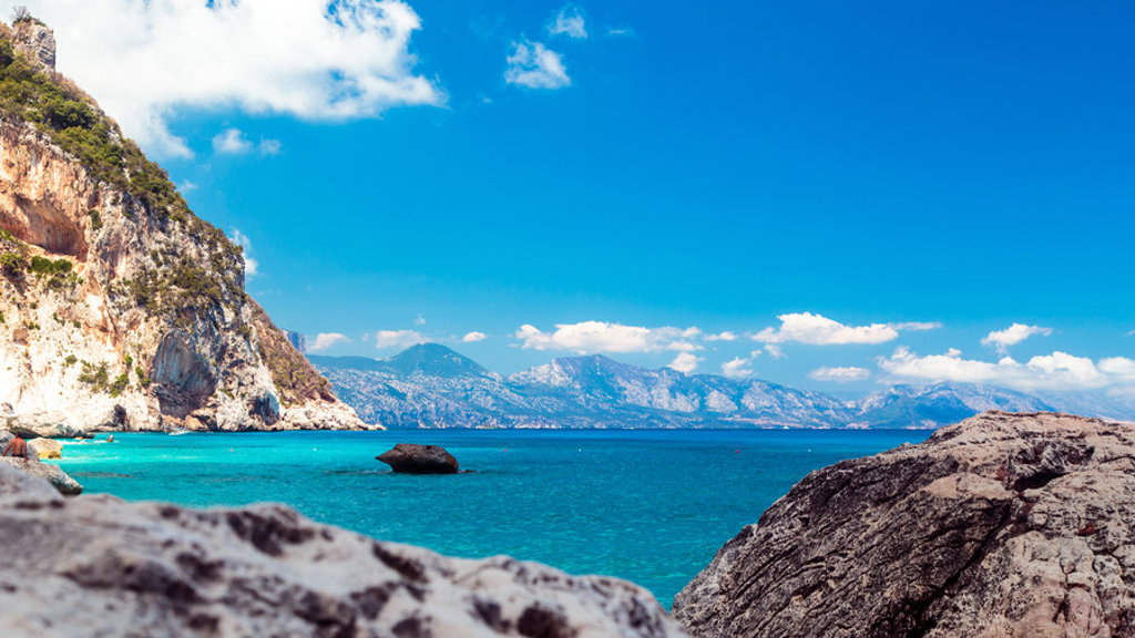 Rotsachtige kust met helderblauwe zee en bergen op de achtergrond op Sardinië, Italië.