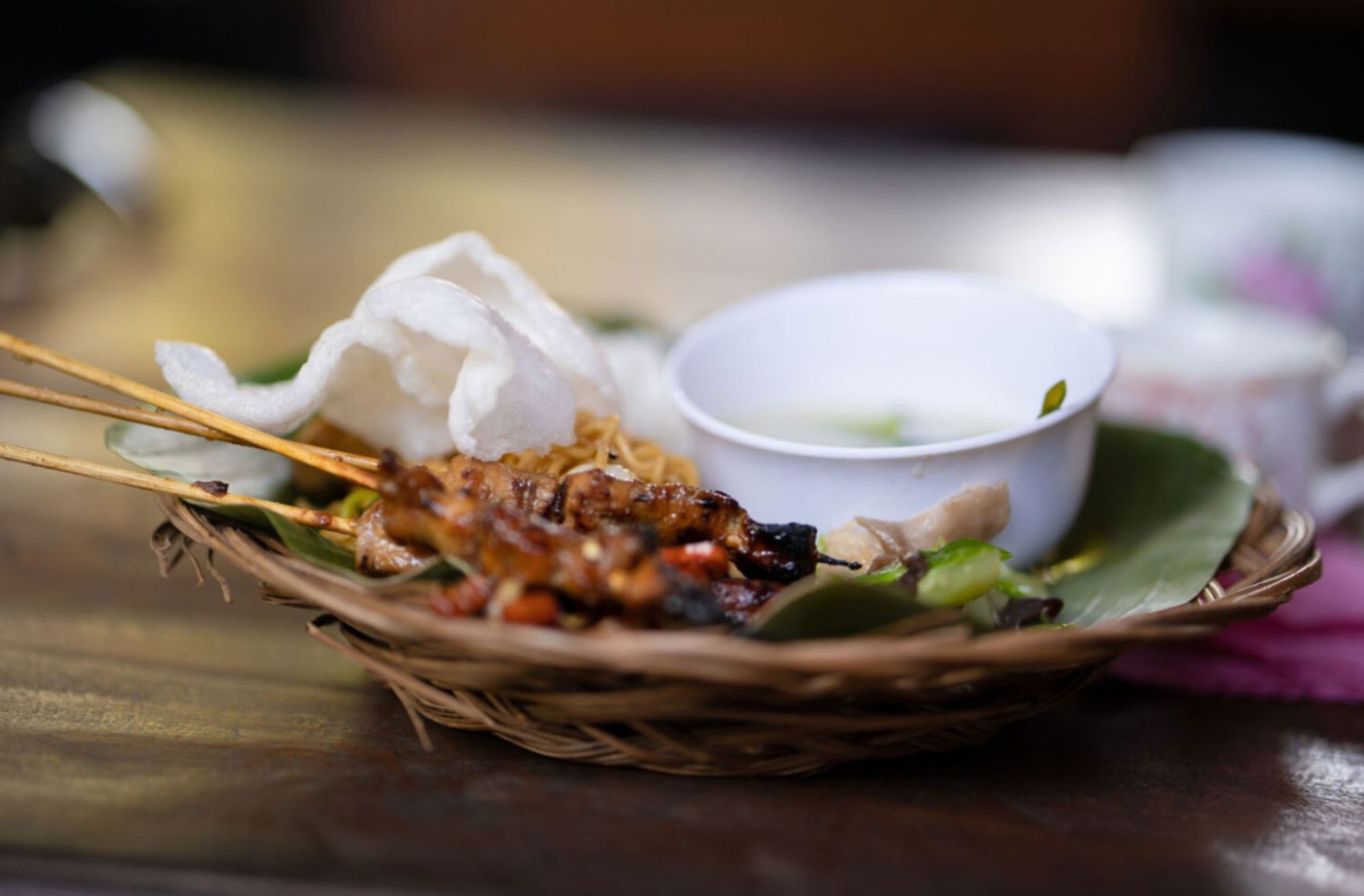 Indonesische saté met pindasaus en kroepoek, geserveerd in een rieten mandje.