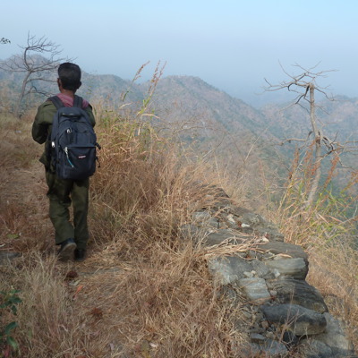 Wandelaar met rugzak op bergpad richting Kumbhalgarh, met uitzicht over heuvels en valleien.