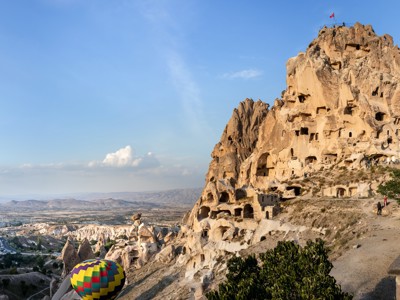 Uitzicht op het rotskasteel van Uçhisar in Cappadocië met uitgehouwen grotwoningen en een luchtballon in de vallei.