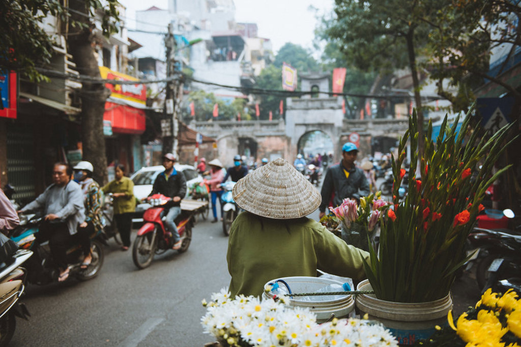 Bloemenverkoopster met kegelvormige hoed in het verkeer van Hanoi, tijdens Familiereis Vietnam Kort.