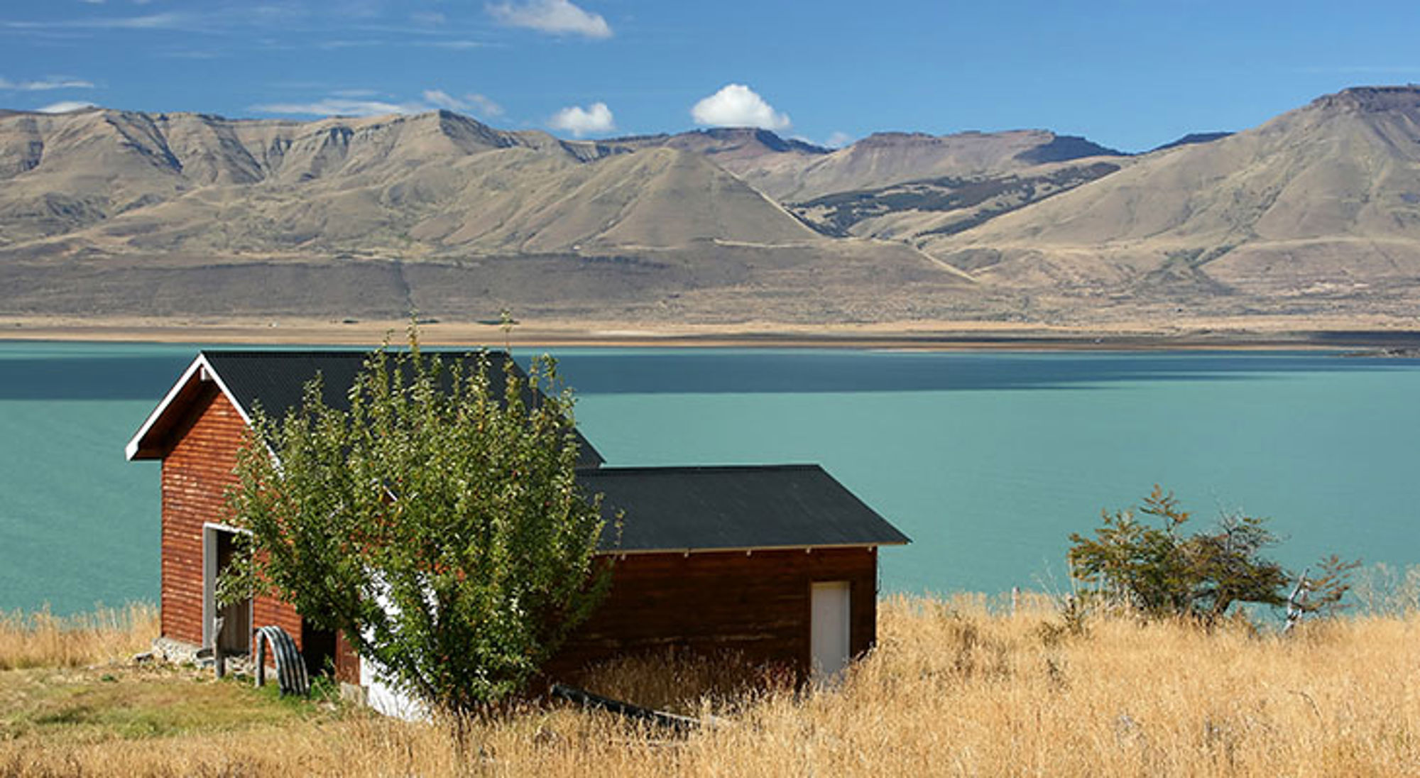 Huis aan een meer met bergen bij El Calafate Rood houten huisje aan een turkoois meer met bergen op de achtergrond in Patagonië.