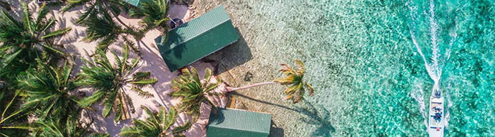 palmbomen en strandhuisjes aan de kust van Belize met een boot op helderblauw water.