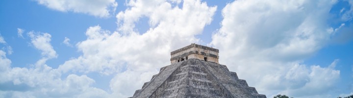 Piramide El Castillo in Chichén Itzá, Mexico, met bezoekers op het grasveld onder een blauwe lucht.