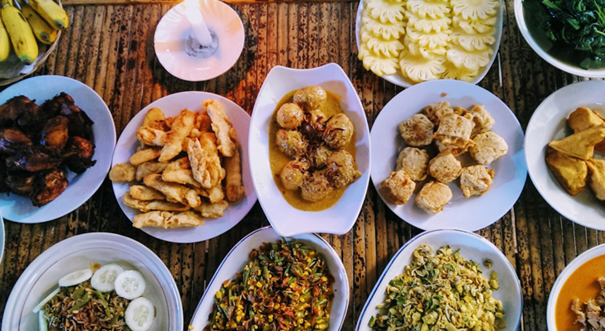 Indonesische rijsttafel met diverse gerechten op tafel, waaronder saté, groenten en curry.