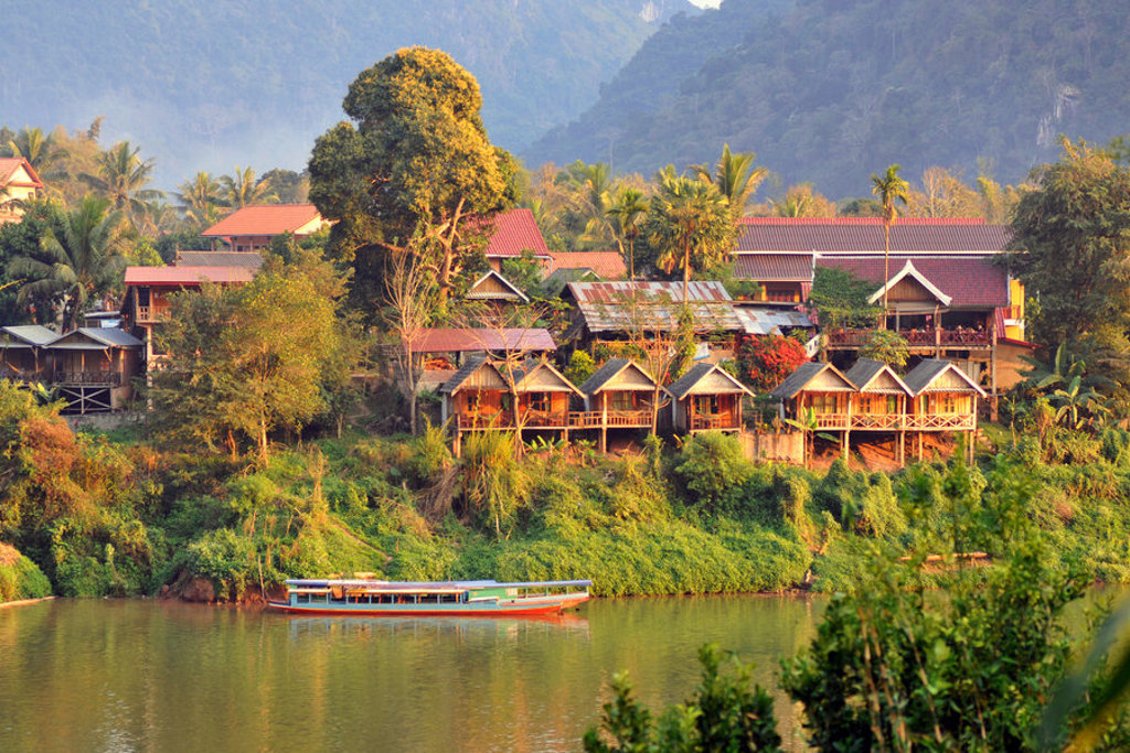 Rivierdorp met houten huisjes en boot bij zonsondergang tijdens familiereis Thailand, Laos en Cambodja.