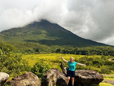 Reiziger bij de Arenal-vulkaan in Costa Rica, met groene vallei en wolken rond de top.