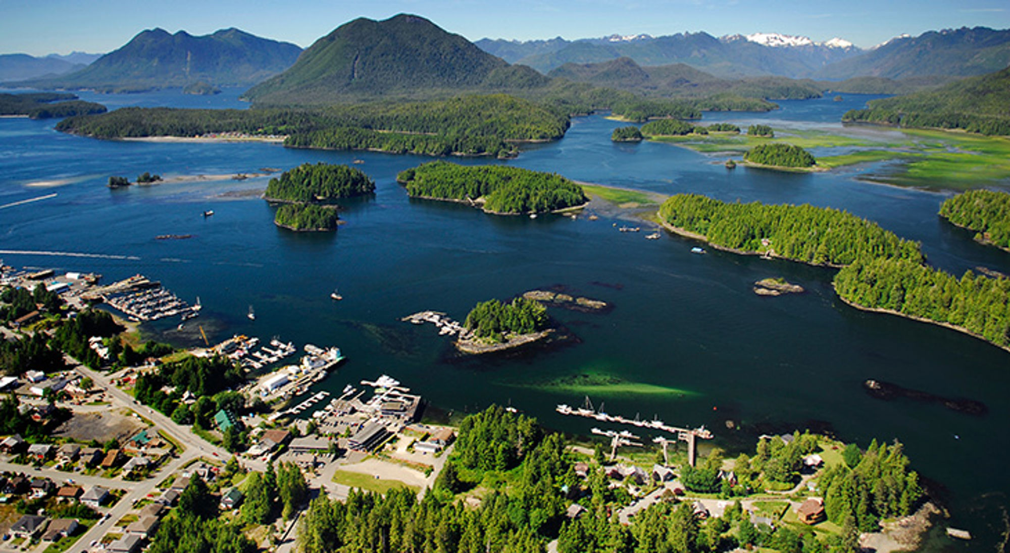een kustplaats met haven, groene eilanden en bergen aan een blauwe baai.