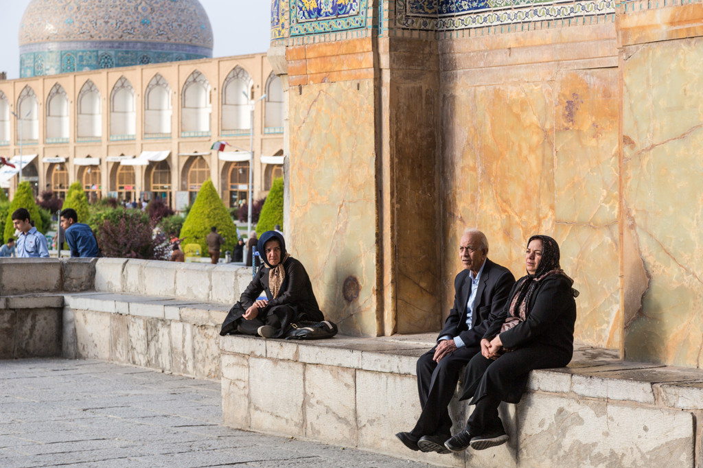 Bezoekers zitten bij een moskee met blauwe koepel op het plein van Isfahan tijdens een rondreis Iran.