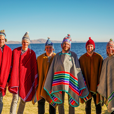 Groep reizigers in kleurrijke poncho’s bij het Titicacameer tijdens een 22-35ers groepsrondreis Peru.