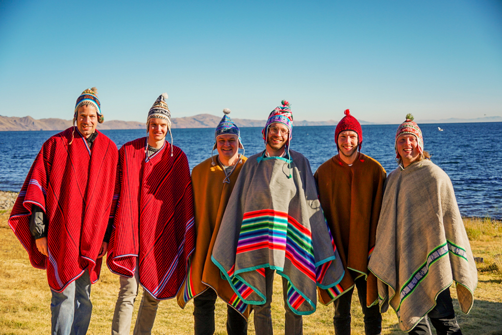 Groep reizigers in kleurrijke poncho’s bij het Titicacameer tijdens een 22-35ers groepsrondreis Peru.