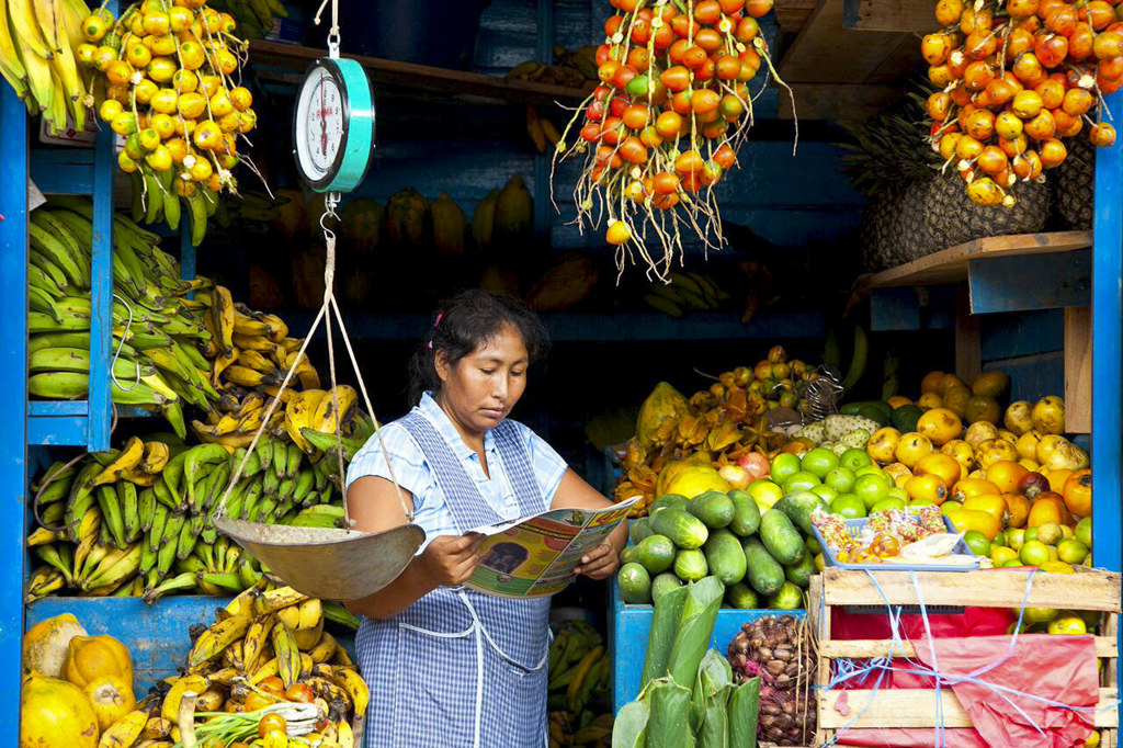 Vrouw bij een fruitkraam op een markt in Peru, omringd door bananen en citrusvruchten.