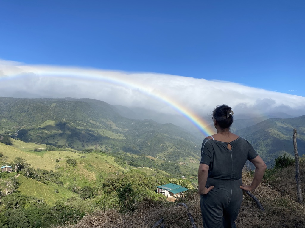 Reiziger kijkt uit over groene bergen in Costa Rica met een regenboog boven de vallei.