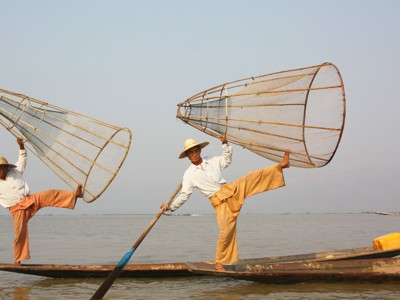 Intha-vissers op het Inlemeer in Myanmar, balancerend op een boot met grote visnetten.