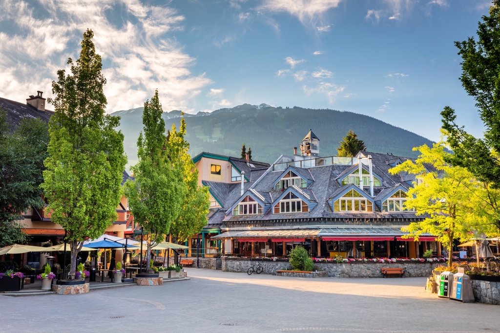 Dorpsplein in Whistler met hotels en terrassen, met de bergen van de Canadese Rockies op de achtergrond.