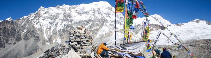 Bergtop met gebedsvlaggen en trekkers tijdens de Langtang Trek in Nepal, met besneeuwde Himalaya op de achtergrond.