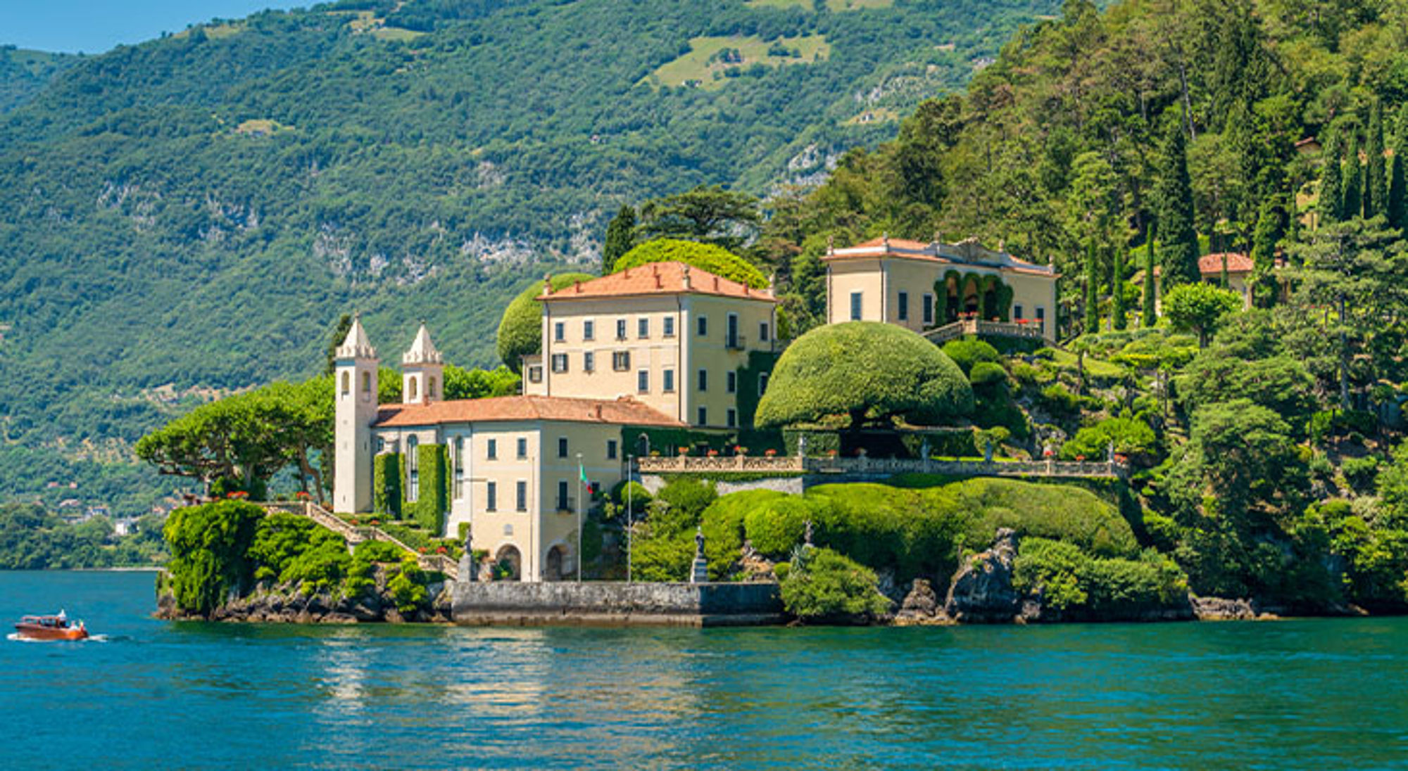 Lago Como Villa en tuinen op een schiereiland aan het Comomeer, met bergen op de achtergrond.