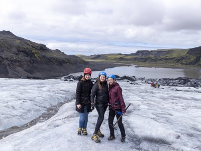 Gletsjerwandeling in IJsland: drie reizigers met helm en stijgijzers op het ijs, met berglandschap op de achtergrond.
